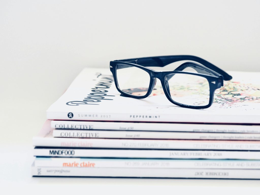 Stylish eyeglasses placed on a stack of colorful fashion magazines, offering a chic and modern vibe.