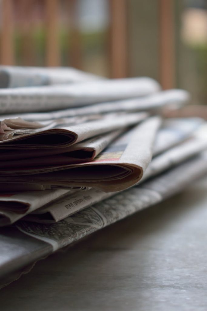 A close-up of a stack of newspapers resting on a desk, symbolizing information and media.