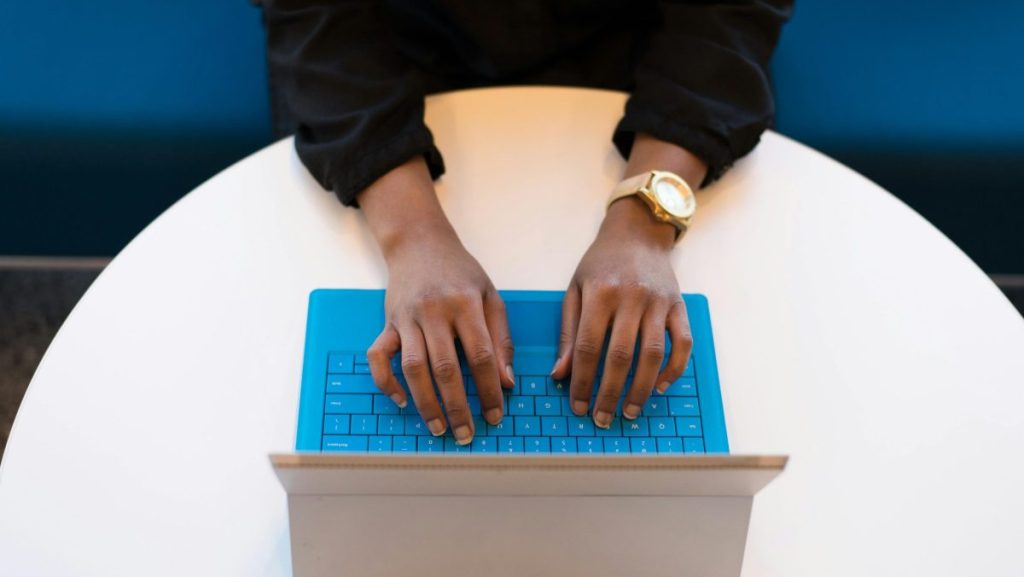 Hands of a person typing on a laptop with a blue keyboard, taken from above, ideal for technology themes.