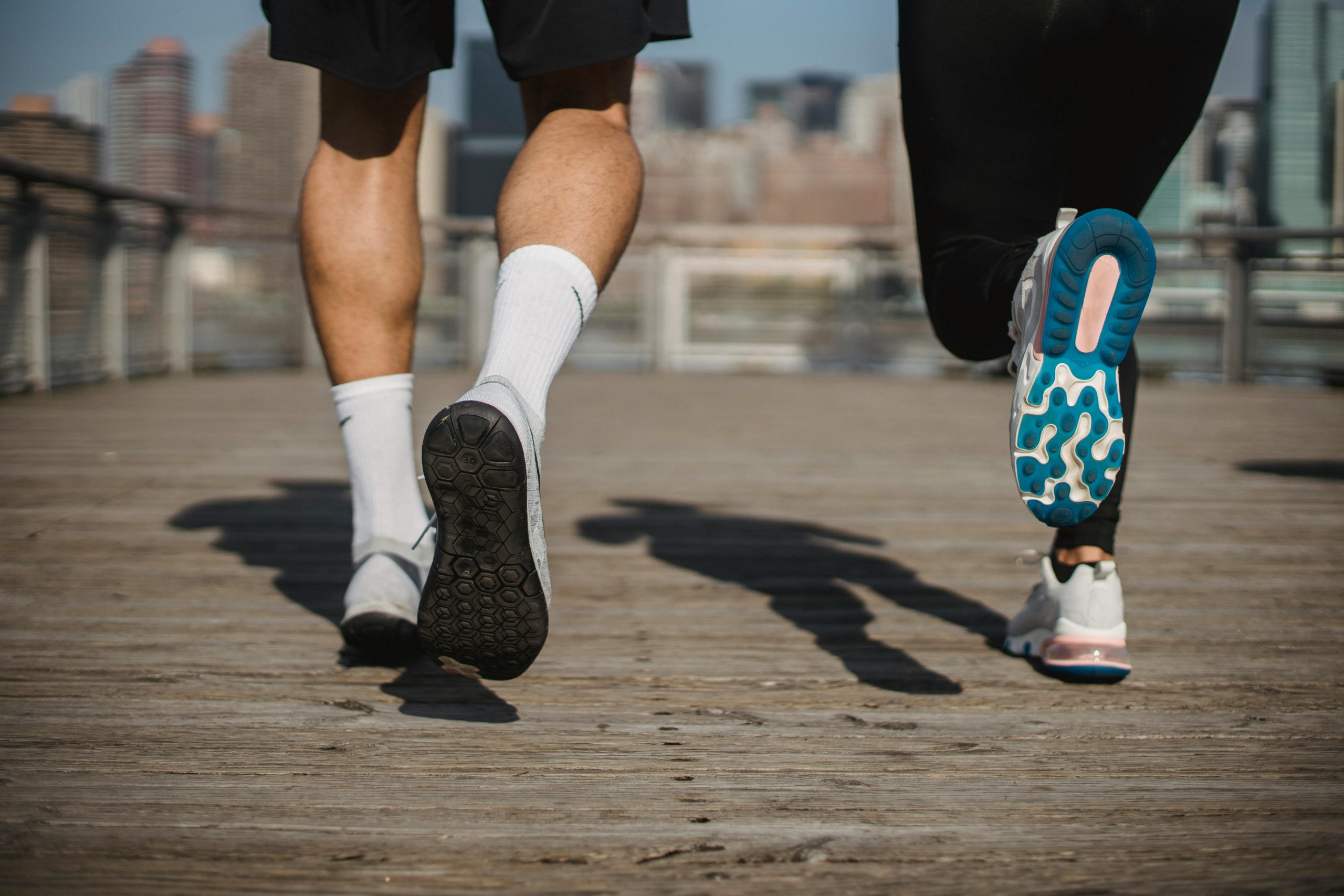 Dynamic shot of two athletes running on a bridge in an urban cityscape, showcasing fitness and determination.