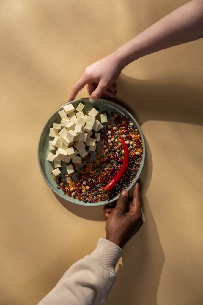 Overhead shot of two hands holding a bowl with tofu cubes, spices, and red pepper, showcasing diversity and flavor.